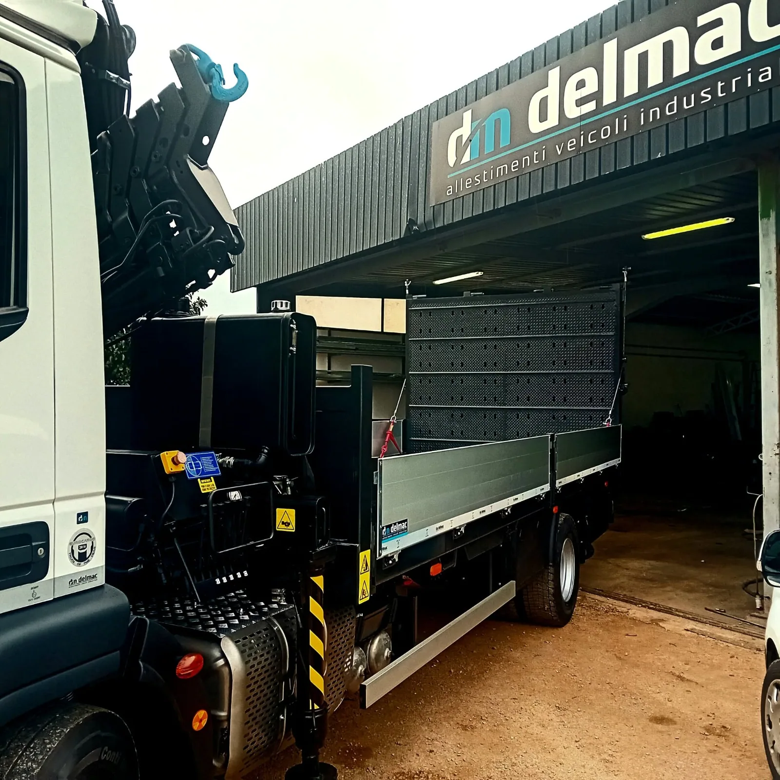 Autocarro Delmac con cassone fisso, gru retrocabina e rampa idraulica per il trasporto di macchine operatrici